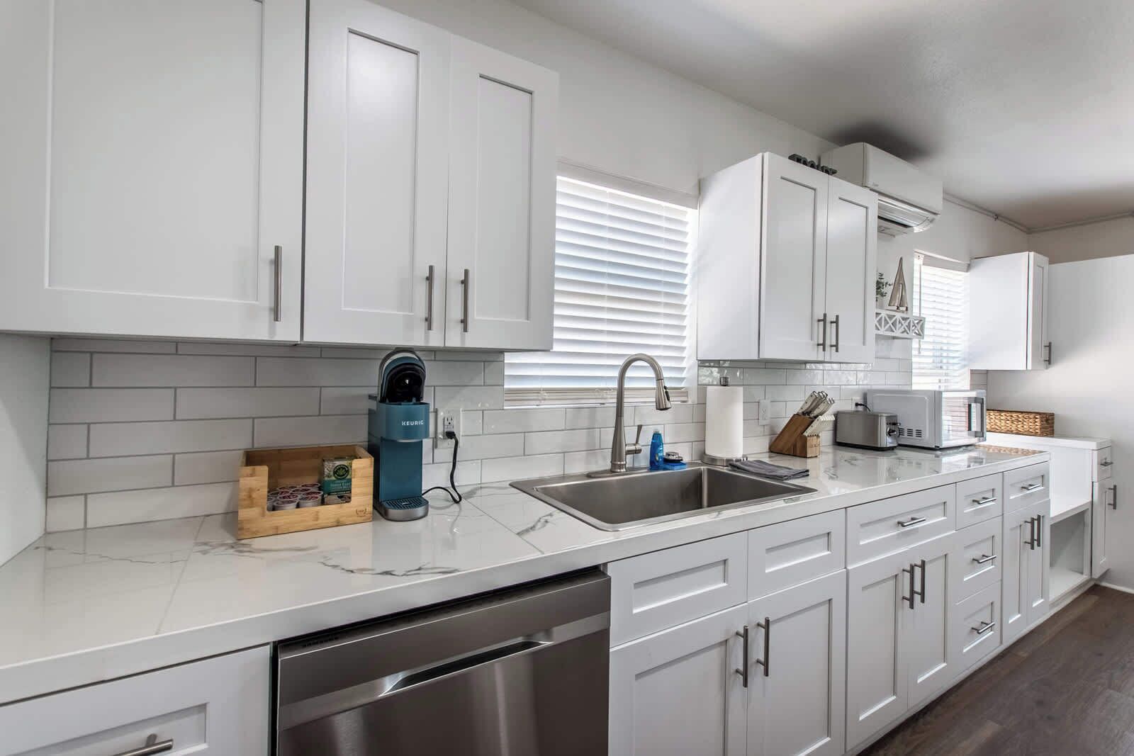 A modern kitchen with white cabinets, a stainless steel sink, and a coffee maker.