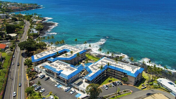 A coastal hotel with multiple buildings, parking, and a view of the ocean. - Kona Reef#B2: Steps from Beach, Fully Remodeled, Ground Floor (Kailua Kona)