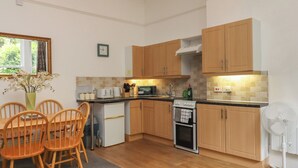 A compact kitchen with wooden cabinets, a microwave, a stove, and a dining area with chairs. - Apartment 2 (Torquay)
