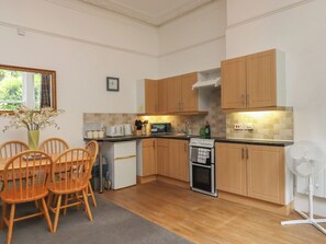 A compact kitchen with wooden cabinets, a microwave, a stove, and a dining area with chairs. - Apartment 2 (Torquay)