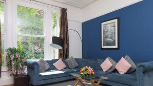A living room with a blue sofa, a glass coffee table, a potted plant, and a painting on the wall. - Apartment 2 (Torquay)