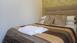 A neatly made bed with a brown and beige striped bedspread, two patterned pillows, and a folded white towel on the footboard. - Apartment 2 (Torquay)