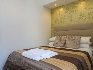 A neatly made bed with a brown and beige striped bedspread, two patterned pillows, and a folded white towel on the footboard. - Apartment 2 (Torquay)