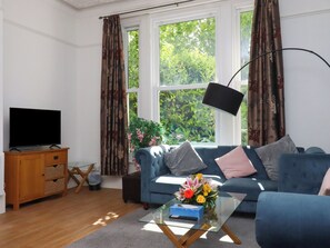 Ein Wohnzimmer mit Fernseher, Sofa, Couchtisch und einem Fenster mit Vorhängen.