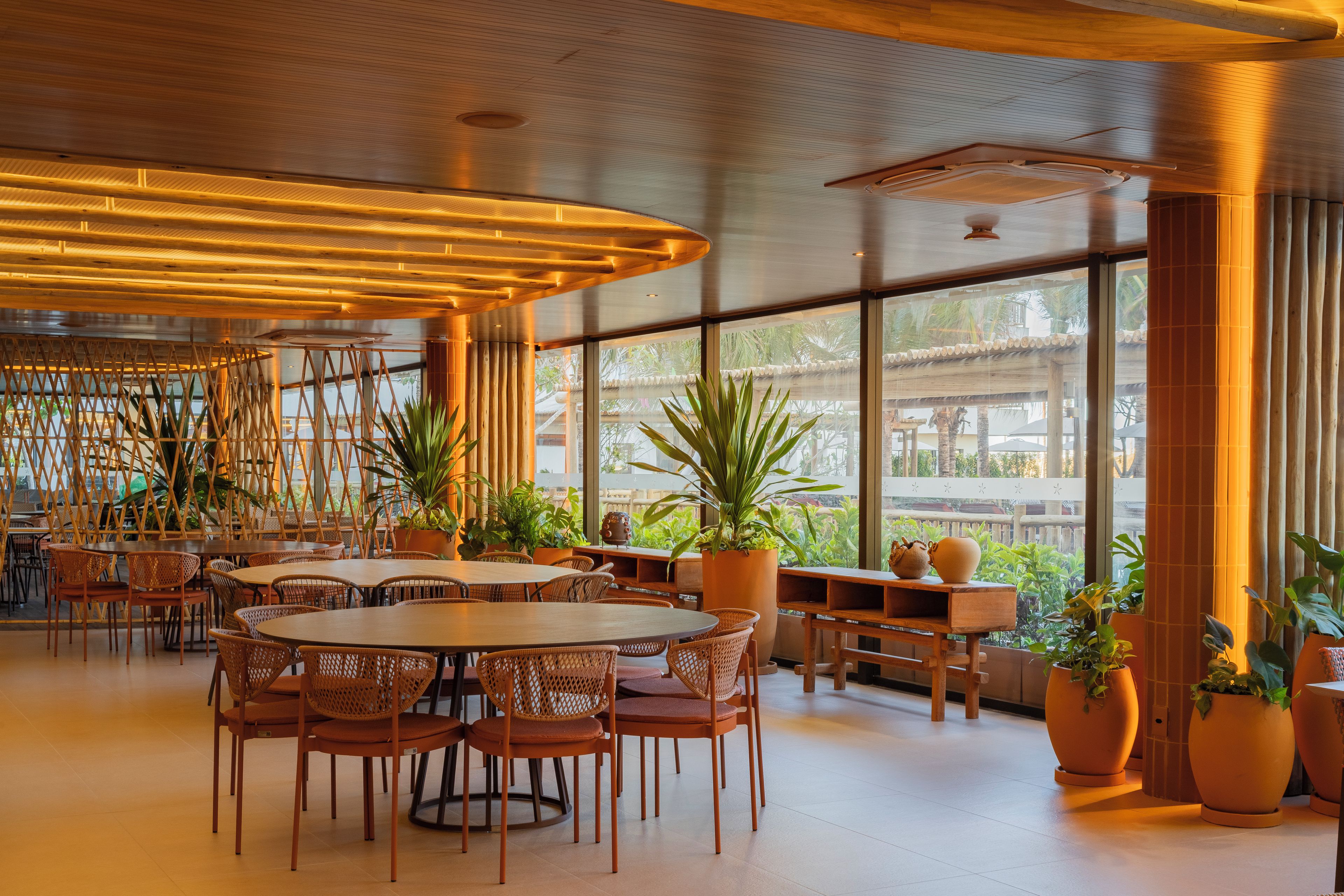 A spacious indoor area with round tables and chairs, large windows, and potted plants.