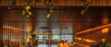 A spacious interior with wooden paneling, a bar area, seating, and potted plants.