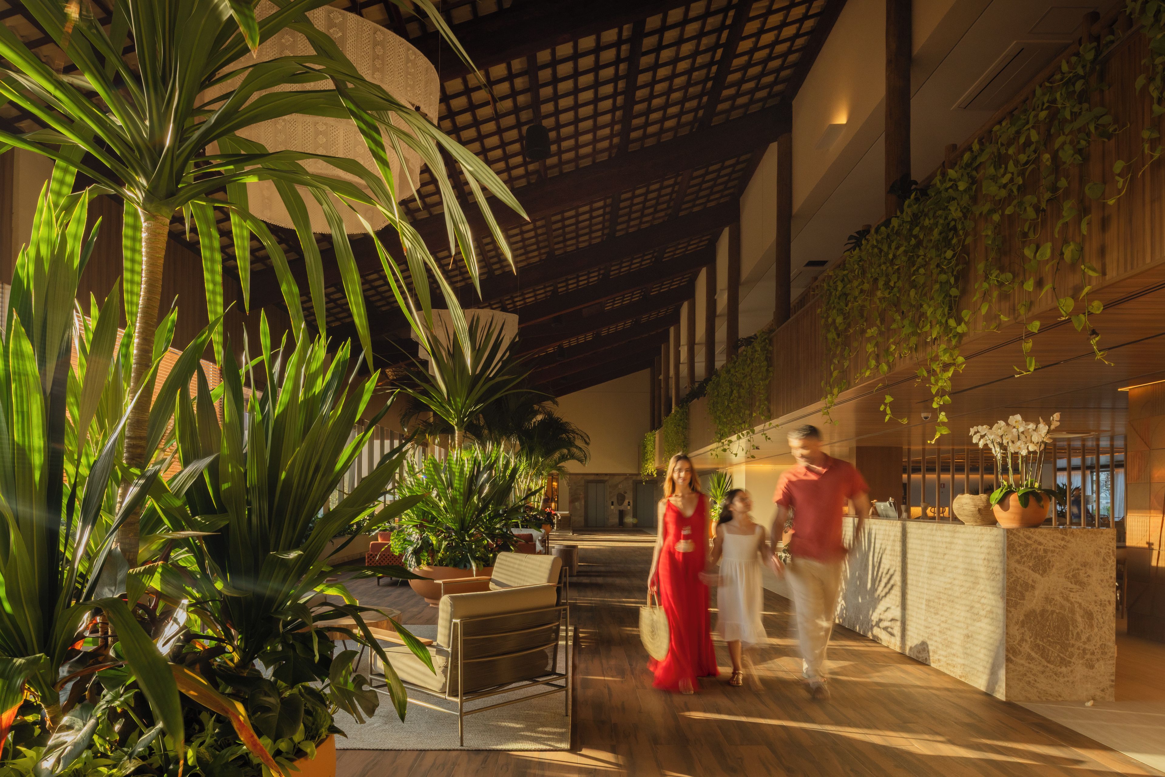 Un espace intérieur vaste et lumineux, avec un plafond haut, de grandes plantes et un comptoir d’accueil moderne.