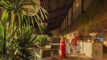 Amplo espaço interno com pé direito alto, plantas grandes e uma moderna mesa de recepção.