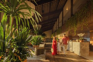 Un espace intérieur vaste et lumineux, avec un plafond haut, de grandes plantes et un comptoir d’accueil moderne.