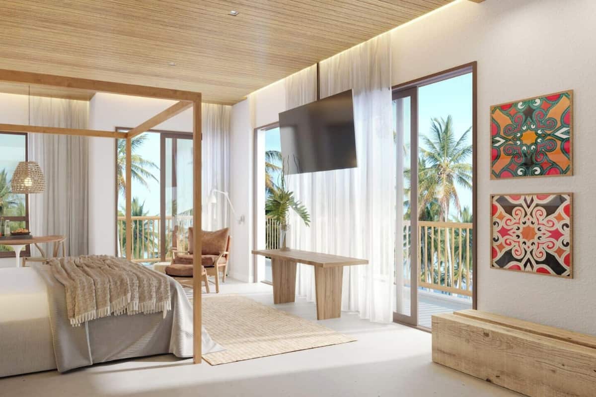 Amplia habitación con una cama grande, televisión, balcón y vistas a la naturaleza tropical.
