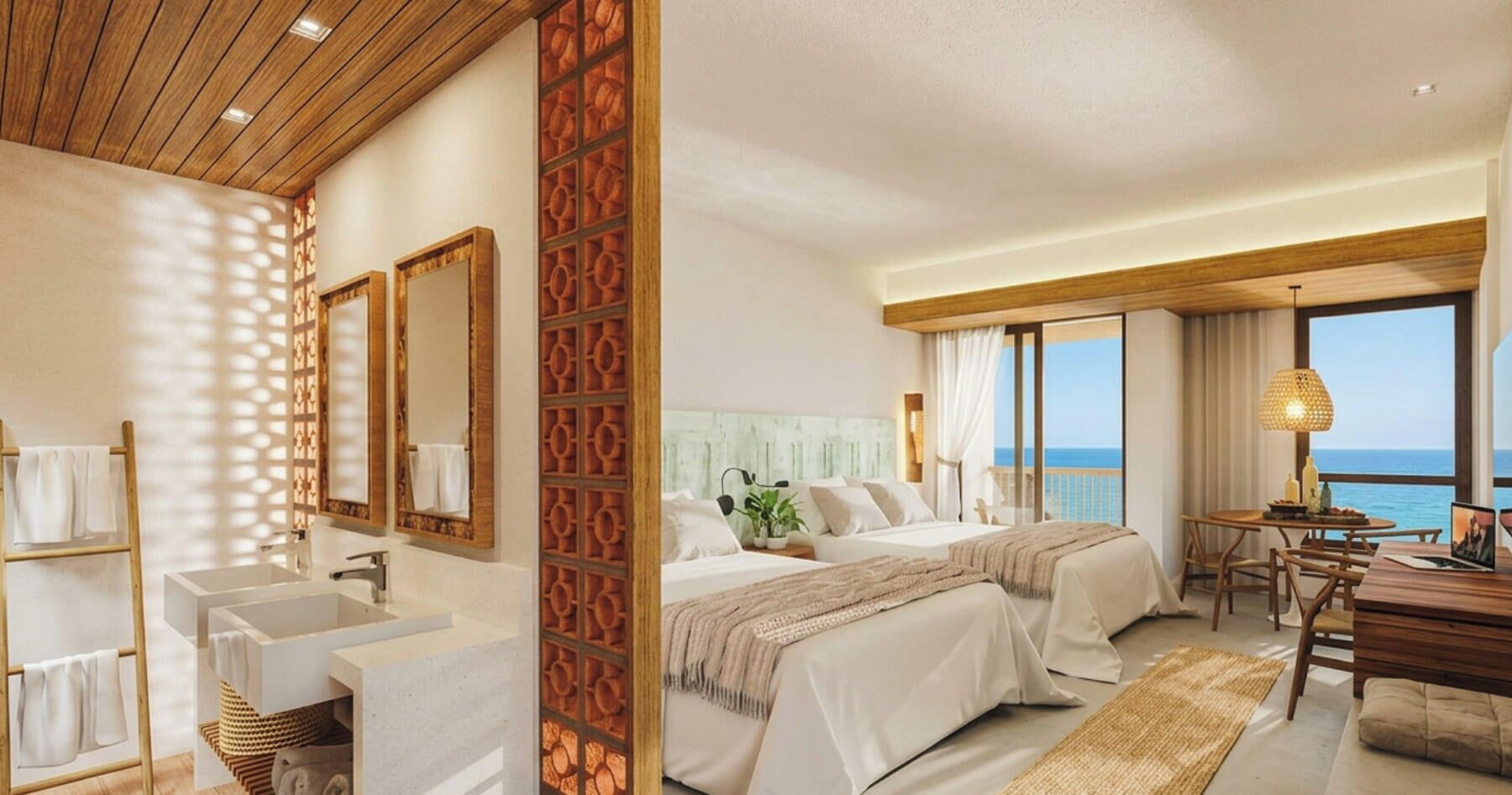 Una habitació d'hotel amb un llit gran, una taula de treball, una cadira, un bany amb un lavabo i un mirall, i vista al mar.