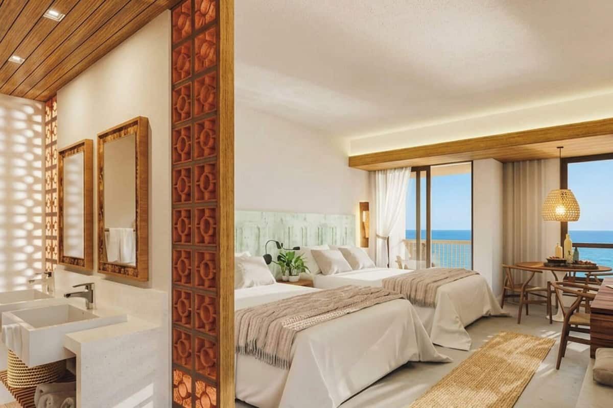 Un cuarto de hotel con una cama grande, un escritorio, una silla, un baño con lavamanos y espejo, y vista al mar.