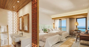 A hotel room with a large bed, a desk, a chair, a bathroom with a sink and mirror, and a view of the sea.