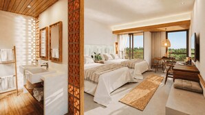 Habitación de hotel con una cama grande, un escritorio, una silla, un ventanal con vistas y un baño con lavamanos y espejo.