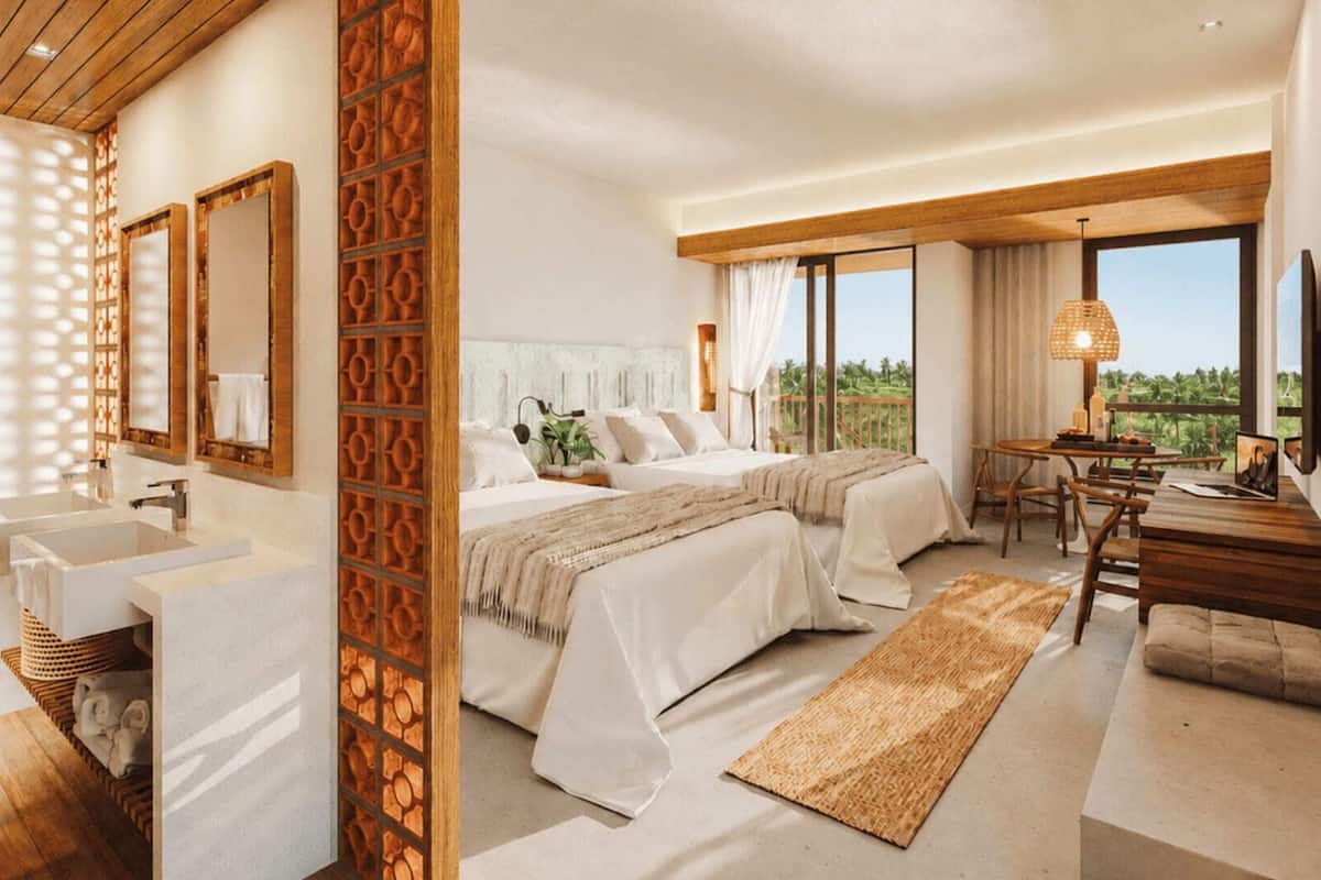 Habitación de hotel con una cama grande, un escritorio, una silla, un ventanal con vistas y un baño con lavamanos y espejo.