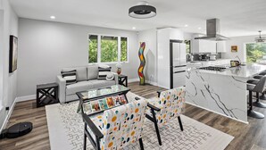 A modern kitchen with a central island, a dining area with a glass table, and a living room with a sofa and a coffee table. - New Listing--A Woodland Escape--Call for Monthly Rates (Cambria)