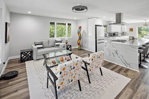A modern kitchen with a central island, a dining area with a glass table, and a living room with a sofa and a coffee table. - New Listing--A Woodland Escape--Call for Monthly Rates (Cambria)