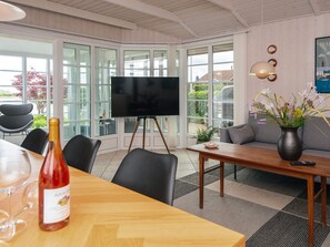 A modern room with a large TV on a tripod stand, a dining table with chairs, a sofa, and a potted plant. - 4 Star Holiday Home in Haderslev (Haderslev)