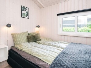 A bedroom with a bed, a bedside table, a wall-mounted lamp, a window with a view of greenery, and a framed plant on the wall. - 4 Star Holiday Home in Haderslev (Haderslev)