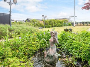 Un jardin avec une statue, une pelouse et un bâtiment en arrière-plan.