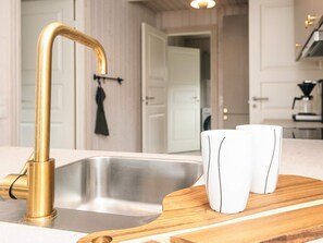 A kitchen with a gold faucet, a stainless steel sink, and a wooden cutting board with two white mugs. - 4 Star Holiday Home in Haderslev (Haderslev)