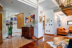 A spacious living area with a staircase, wooden furniture, and artwork on the walls.