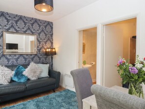 A living room with a dark sofa, a blue rug, a grey armchair, a mirror, and a wall with a patterned wallpaper. - Apartment 4 (Torquay)