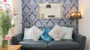 A dark leather sofa with fluffy pillows, a framed mirror, a vase of flowers, and a floor lamp. - Apartment 4 (Torquay)