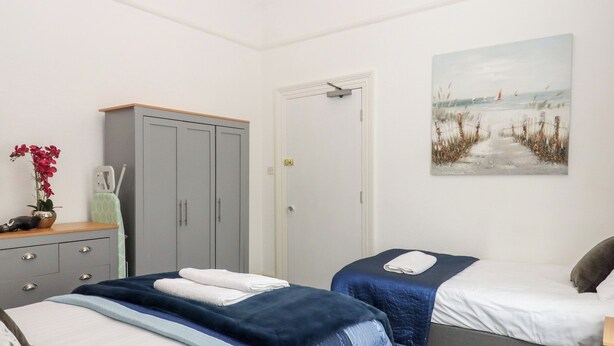 A bedroom with two beds, a wardrobe, a door, and a beach-themed painting. - Apartment 4 (Torquay)