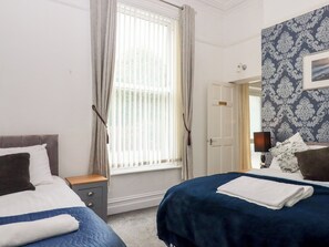 Ein Hotelzimmer mit zwei Betten, einem Fenster mit Vorhängen, einer Tür und einer Wand mit Muster.