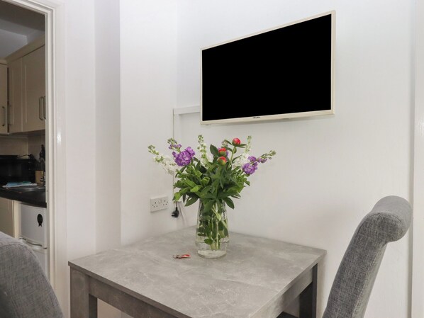 Ein kleiner Tisch mit Blumenvase, ein Wand-Fernseher und ein Stuhl.