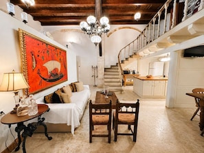 A cozy living room with a sofa, a dining table, and chairs, a staircase, and a kitchen area. - Venetian Palace - Rooftop & Jacuzzi - 5 Bedrooms (Chania)