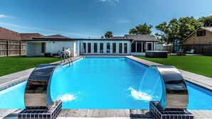 A rectangular swimming pool with a clear blue water surface, surrounded by a wooden deck and a grassy lawn. - Pearl Grand on Ocean (Corpus Christi)