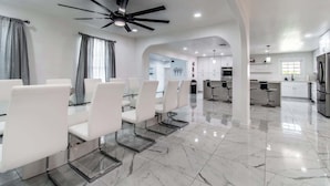 A spacious dining area with a modern ceiling fan, a kitchen with stainless steel appliances, and a clean, polished floor. - Pearl Grand on Ocean (Corpus Christi)