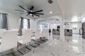 A modern kitchen with stainless steel appliances, a dining area with white chairs and a glass table, and a ceiling fan. - Pearl Grand on Ocean (Corpus Christi)