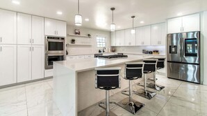 A modern kitchen with white cabinets, stainless steel appliances, and a central island with bar stools. - Pearl Grand on Ocean (Corpus Christi)