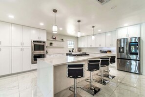 A modern kitchen with white cabinets, stainless steel appliances, and a central island with bar stools. - Pearl Grand on Ocean (Corpus Christi)