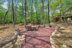 Une zone boisée avec une table et des chaises au centre, entourée d’arbres et d’une structure couverte en arrière-plan.
