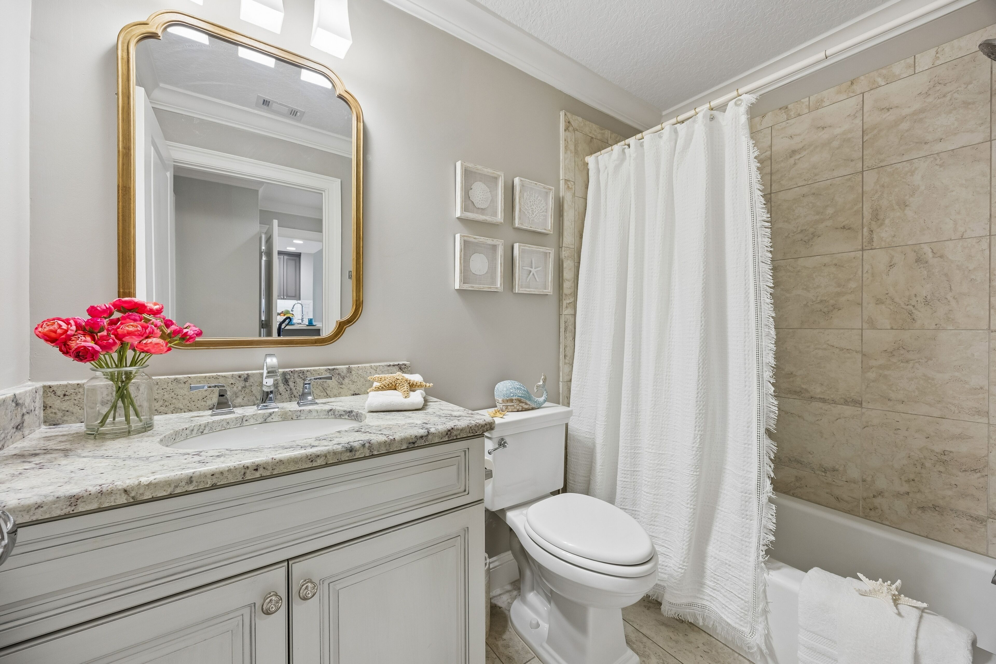 A bathroom with a marble sink, white toilet, and a shower with a beige tiled wall.