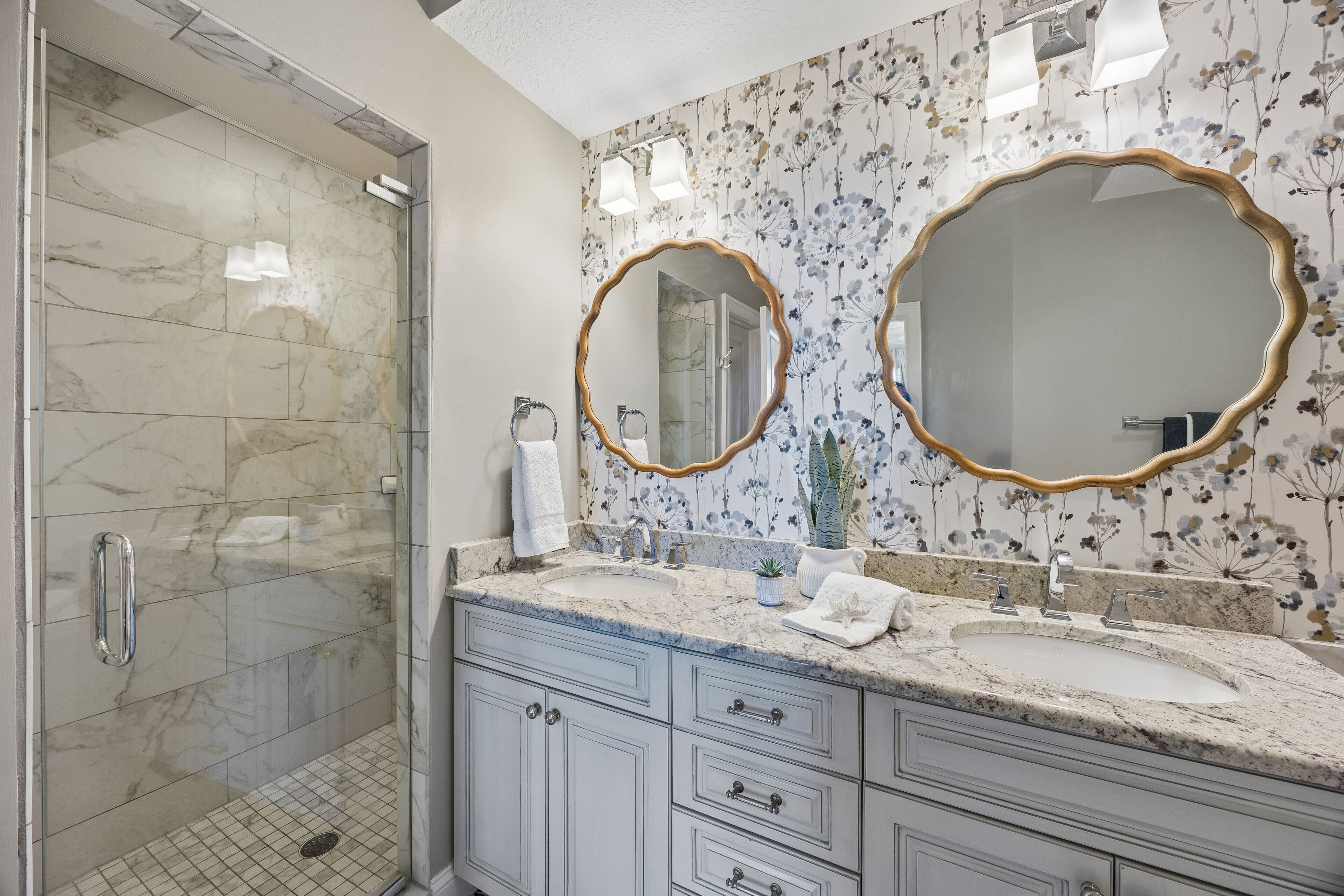 A bathroom with a shower, two sinks, and a large mirror with a gold frame.