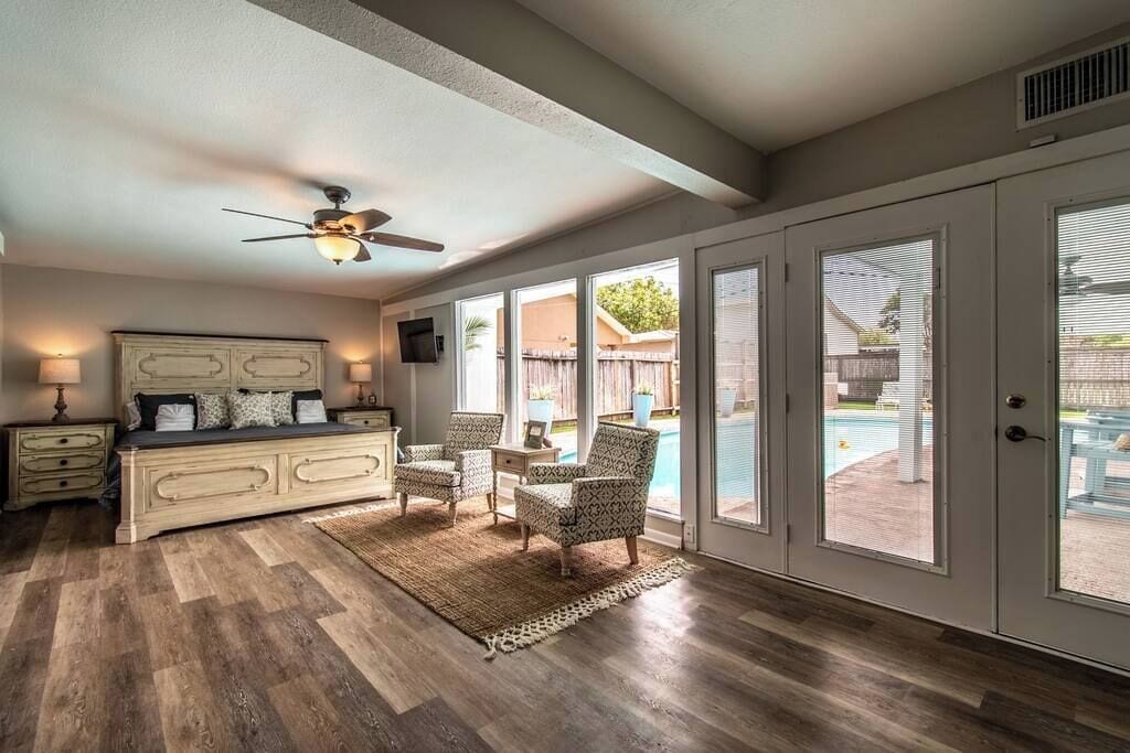 A bedroom with a bed, bedside tables, a ceiling fan, and large windows with a view of a backyard.