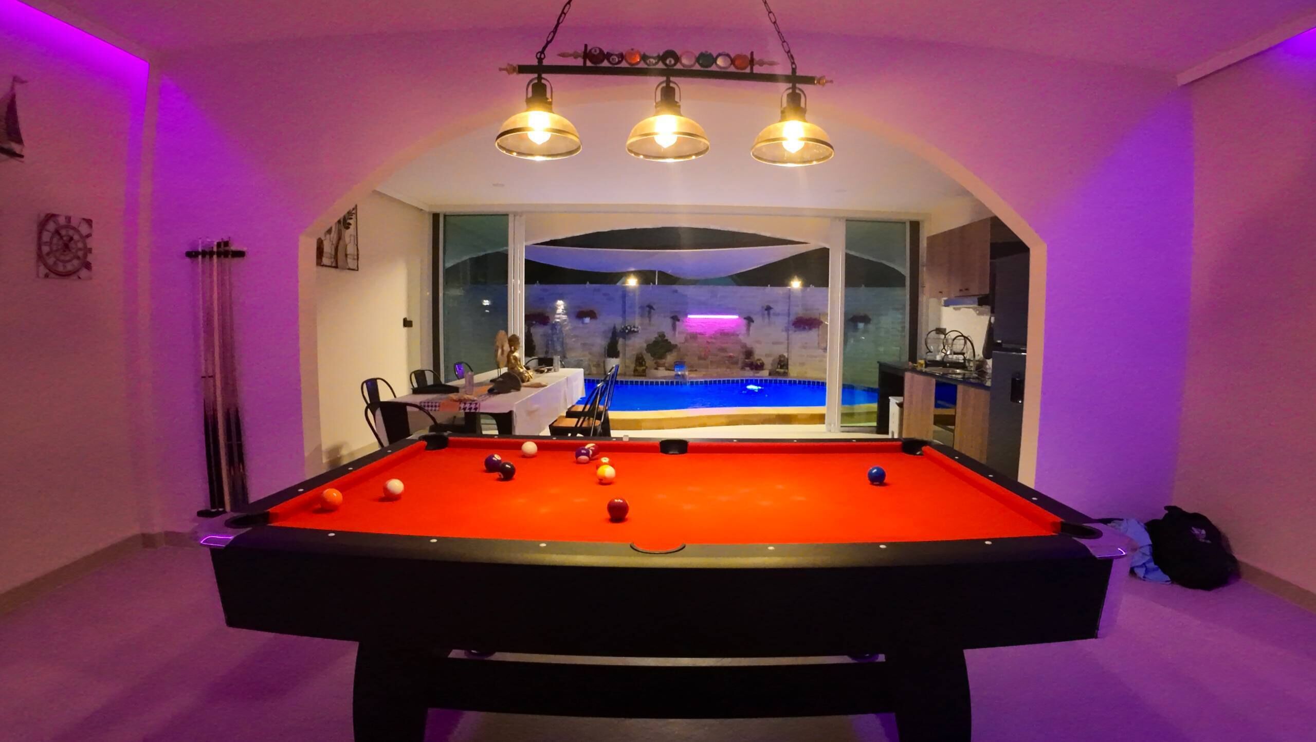 A pool table with balls, a dining area, and a view of a pool outside.