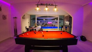 Ein Billardtisch mit Kugeln, ein Essbereich und Blick auf ein Schwimmbad.