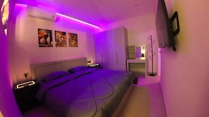 Ein modernes Schlafzimmer mit Bett, Nachttischen, einem Kleiderschrank, einem Spiegel und einem an der Wand befestigten Fernseher.