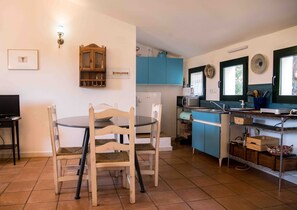 Uma cozinha compacta com armários azuis, uma mesa de jantar com cadeiras, um refrigerador pequeno e um micro-ondas.