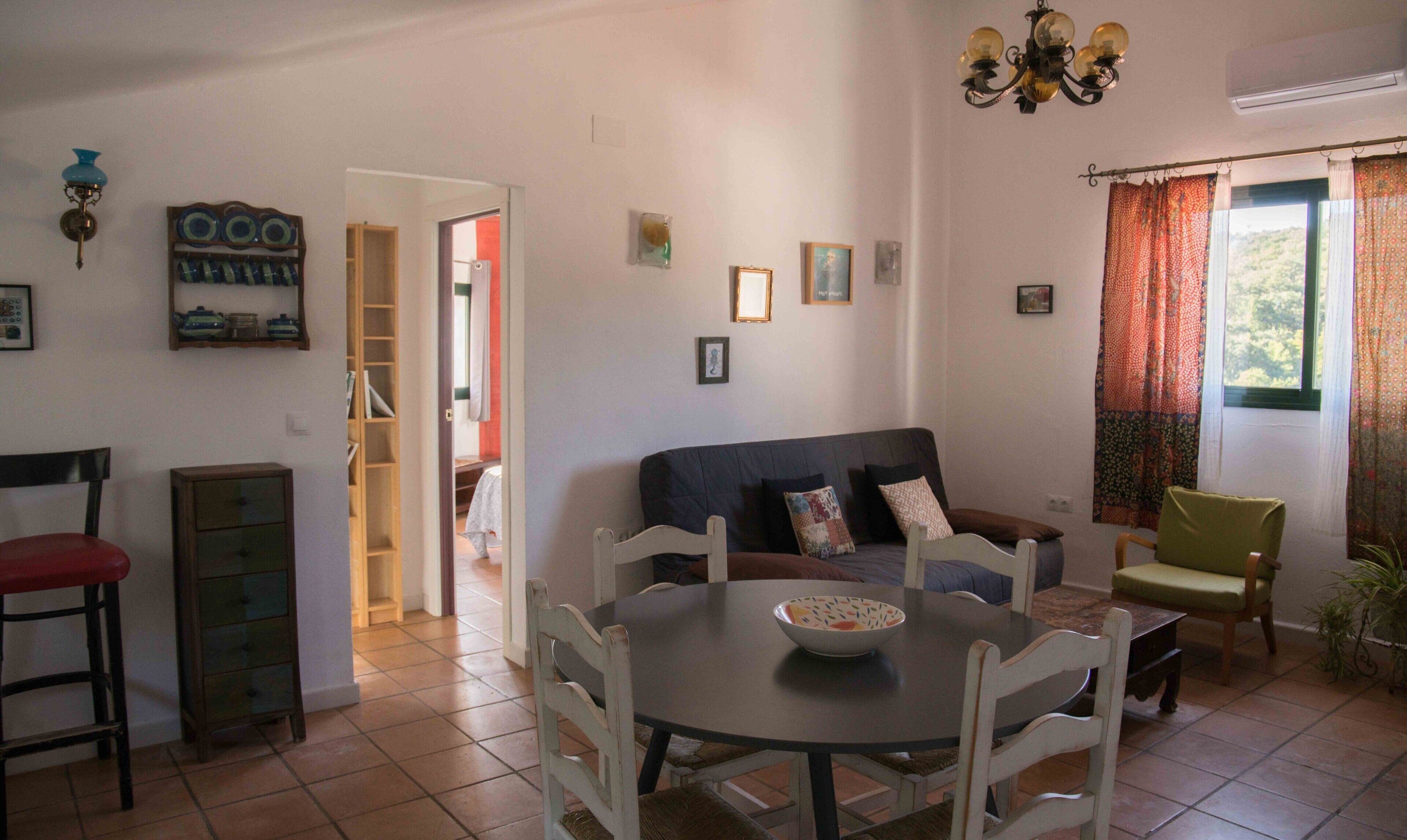 Ein Wohnzimmer mit Sofa, Esstisch, Stühlen, einer Chandelier und einem Fenster mit Vorhängen.