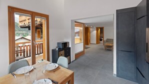 A modern kitchen with dark cabinetry, a dining area with a wooden table and chairs, and a view of a wooden deck and mountains in the background. - Charming apartment in an authentic village (Anniviers)