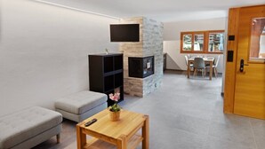 A modern living room with a stone fireplace, a grey sofa, a wooden coffee table, and a dining area with a table and chairs. - Charming apartment in an authentic village (Anniviers)