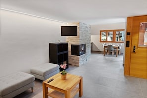 A modern living room with a stone fireplace, a grey sofa, a wooden coffee table, and a dining area with a table and chairs. - Charming apartment in an authentic village (Anniviers)