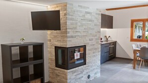 A modern living room with a stone fireplace, a flat-screen TV mounted above it, and a dining area with a table and chairs. - Charming apartment in an authentic village (Anniviers)
